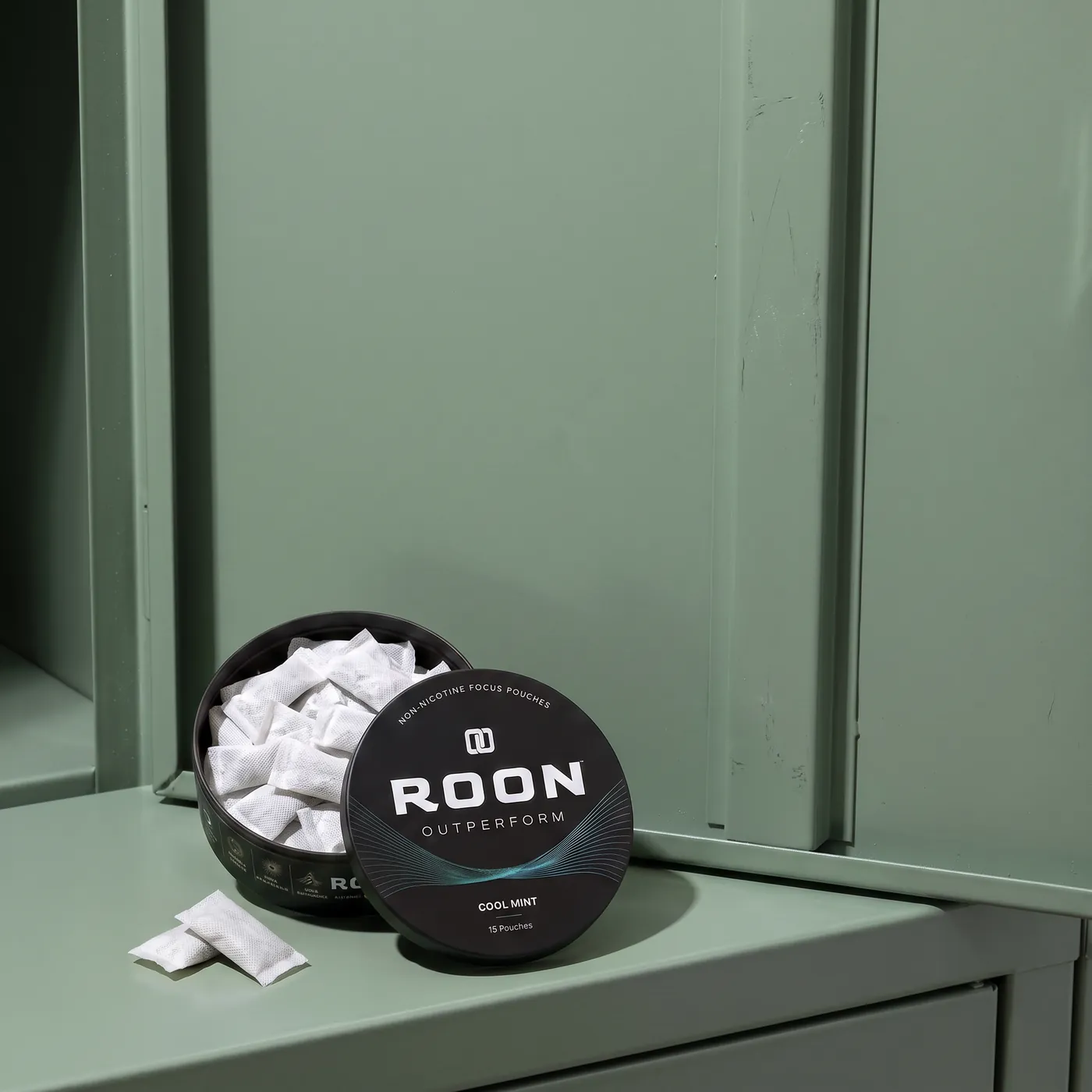 An open tin of Roon Cool Mint pouches on a bench beside a water bottle in a bright gym.