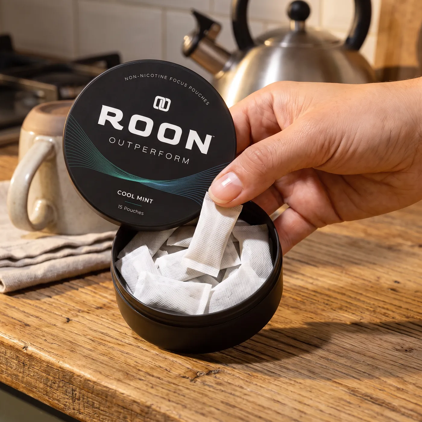 A hand lifting one flat white Roon Cool Mint pouch from an open matte black tin, on a clean cream background.