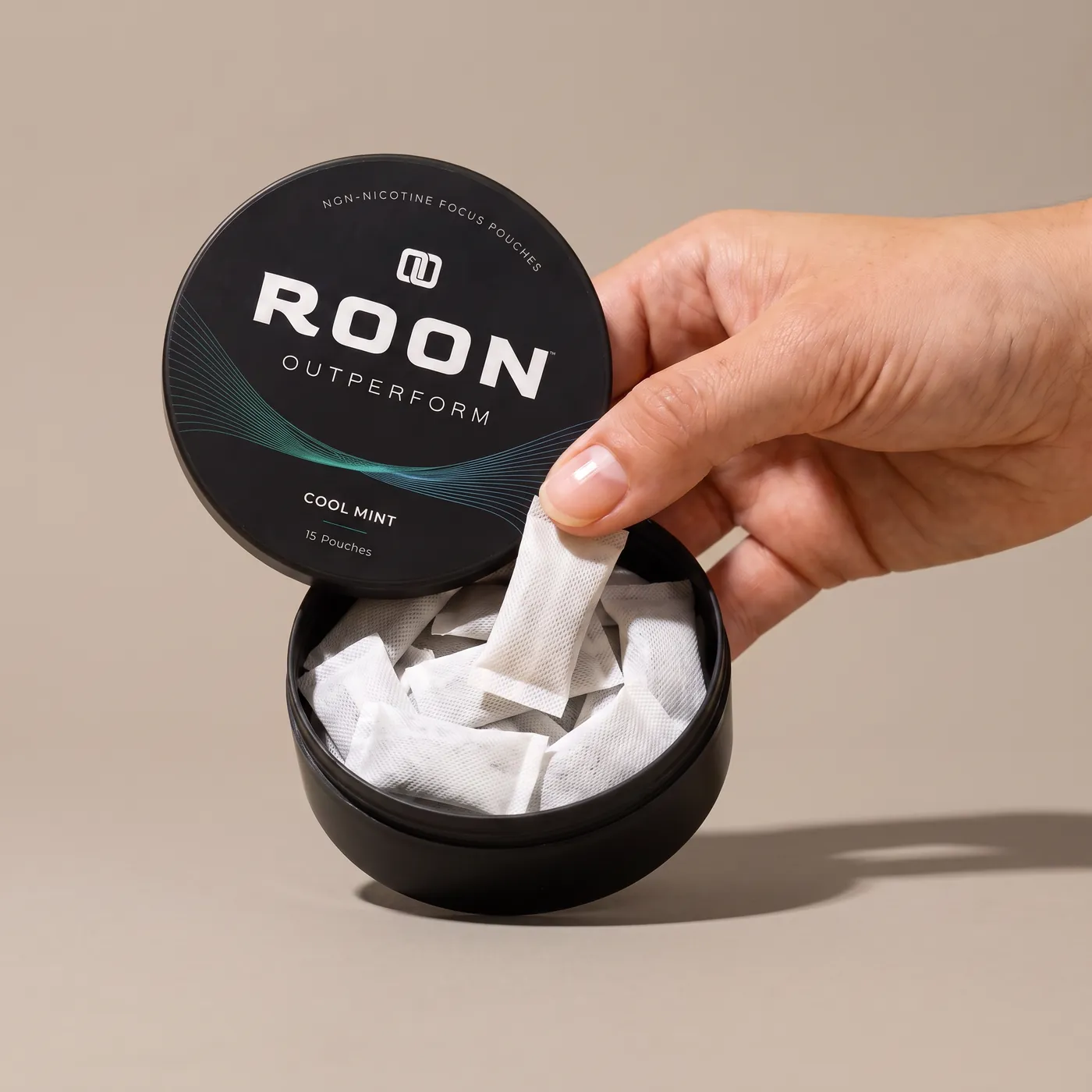 A hand lifting one flat white Roon Cool Mint pouch from an open matte black tin, on a clean cream background.