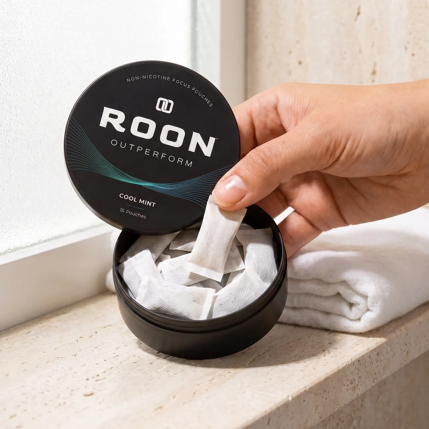 A hand lifting one flat white Roon Cool Mint pouch from an open matte black tin, on a clean cream background.