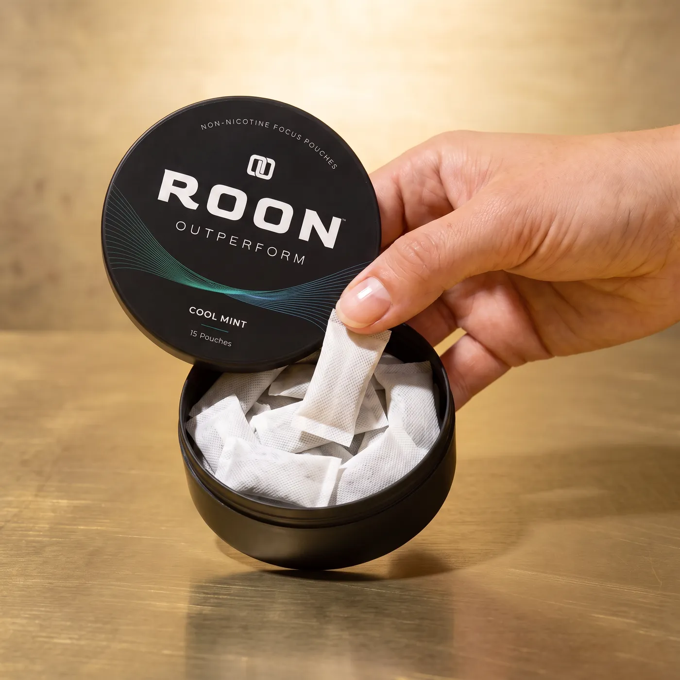 A hand lifting one flat white Roon Cool Mint pouch from an open matte black tin, on a clean cream background.