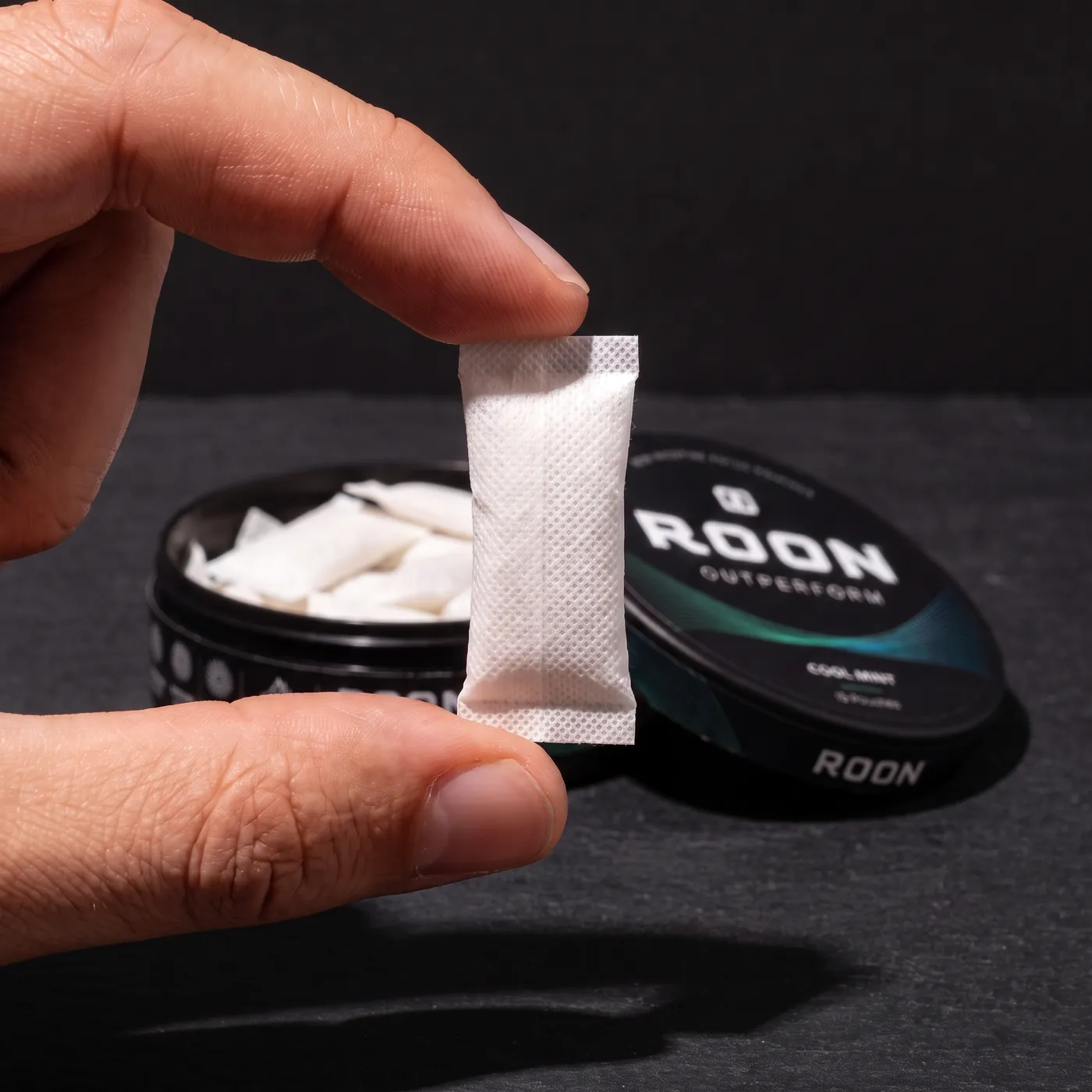 Close view of a single flat white Roon caffeine pouch held between two fingertips, showing the woven fabric.