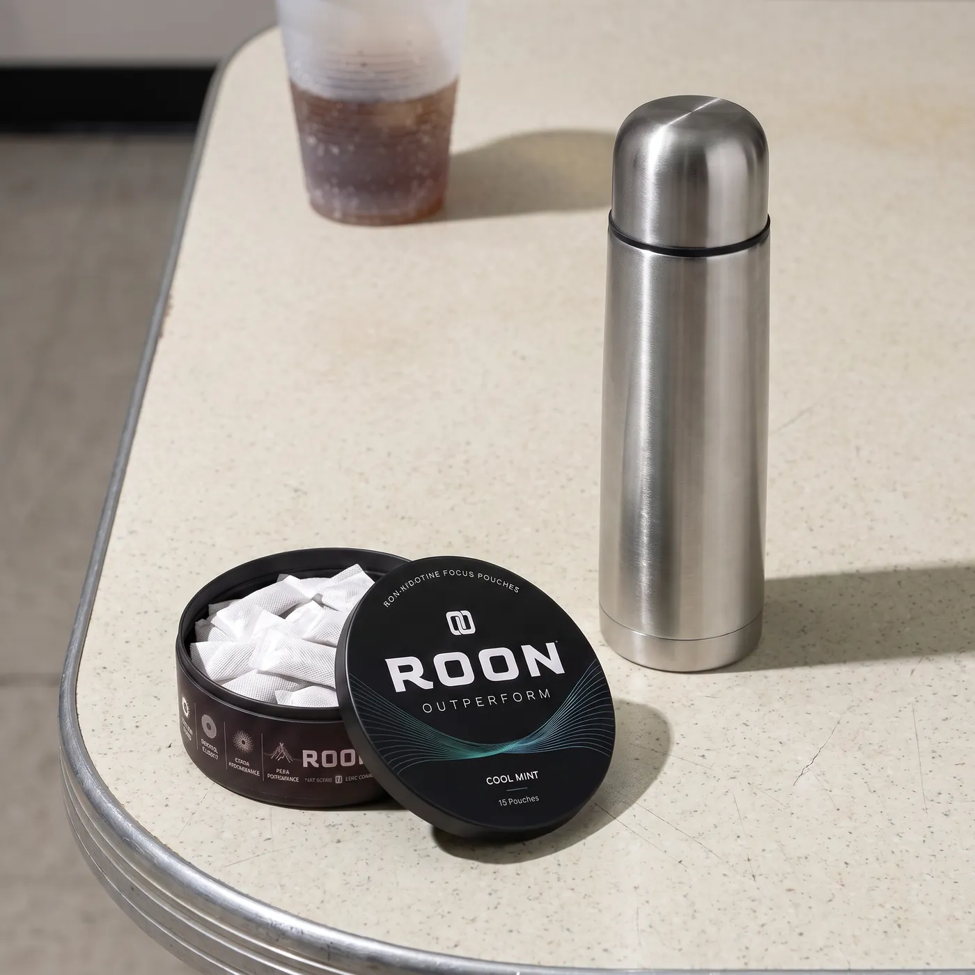 An open tin of Roon Cool Mint pouches on a bright break room counter beside a stainless flask.