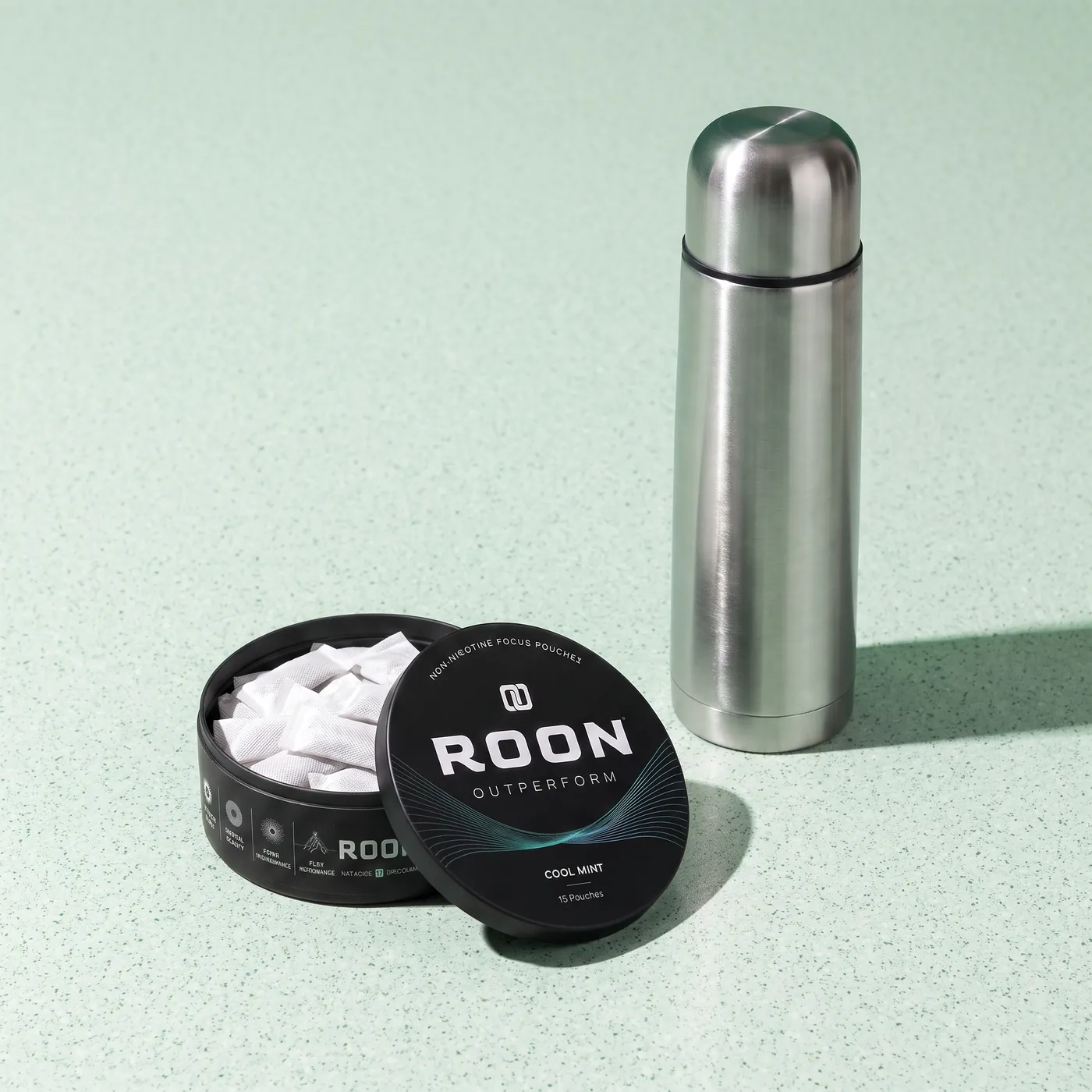 An open tin of Roon Cool Mint pouches on a bright break room counter beside a stainless flask.