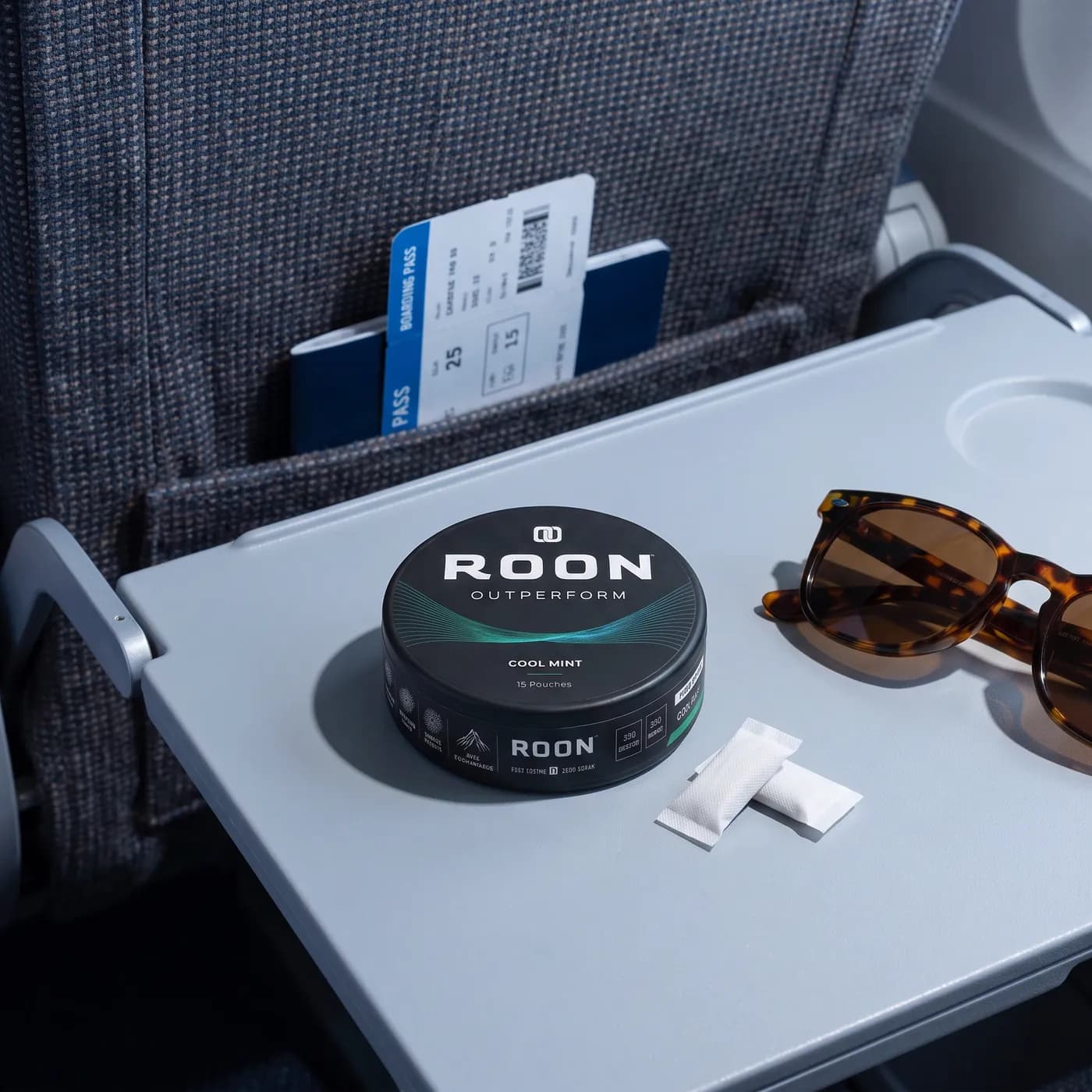 A closed tin of Roon Cool Mint pouches on an aircraft tray table in bright cabin daylight.