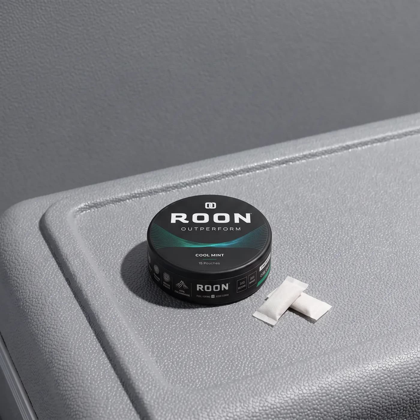 A closed tin of Roon Cool Mint pouches on an aircraft tray table in bright cabin daylight.
