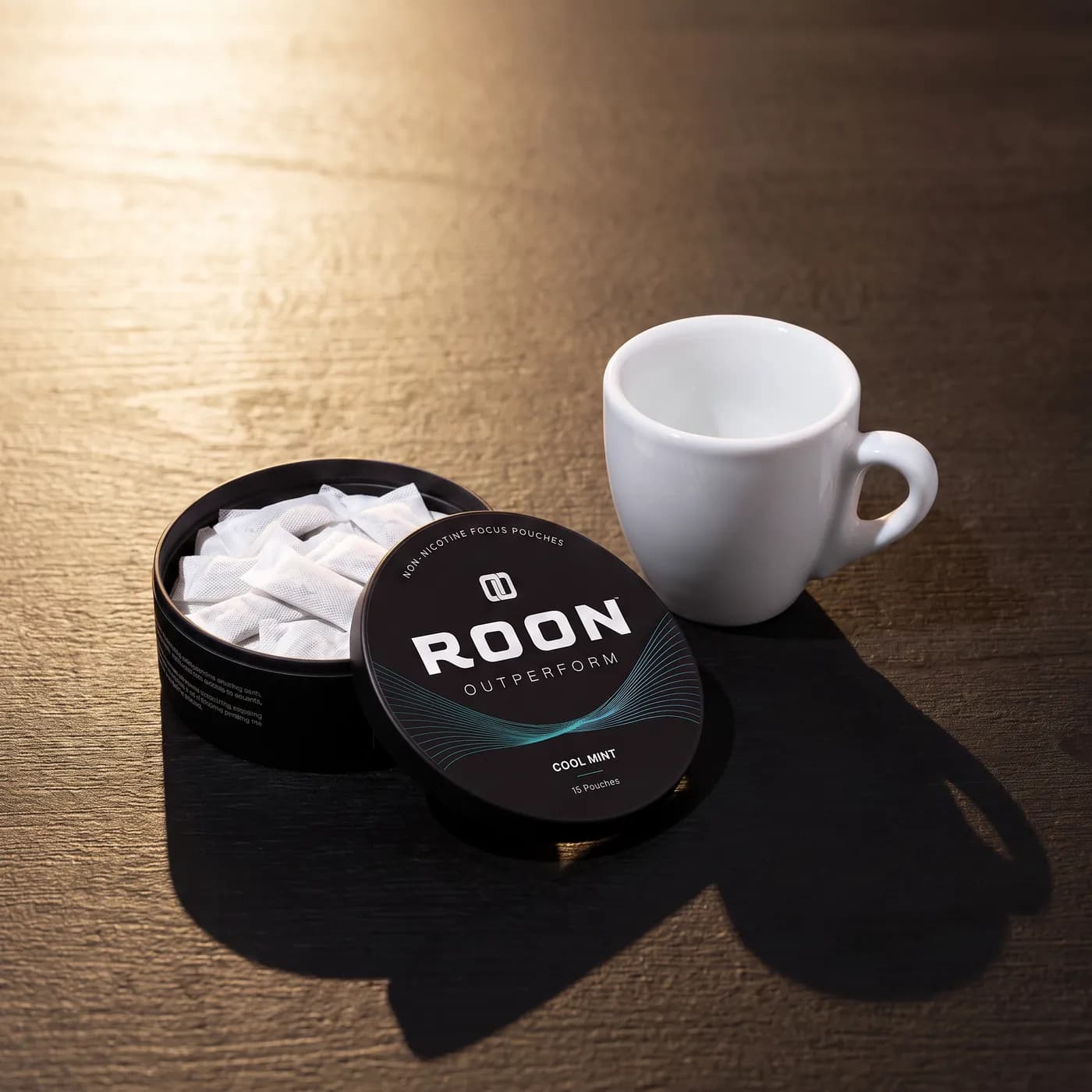 An open tin of Roon Cool Mint pouches beside an empty espresso cup, comparing a pouch to a cup of coffee.