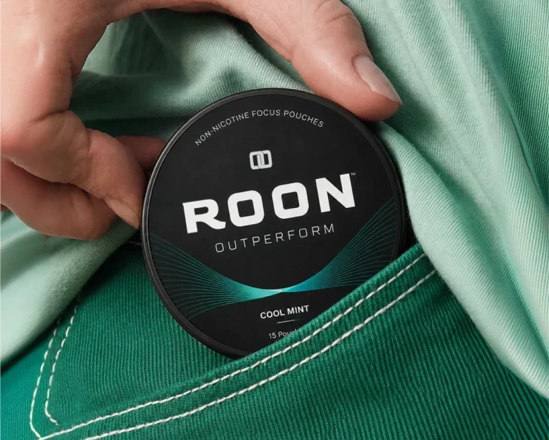 A hand tucking a tin of Roon Cool Mint pouches into a shirt pocket